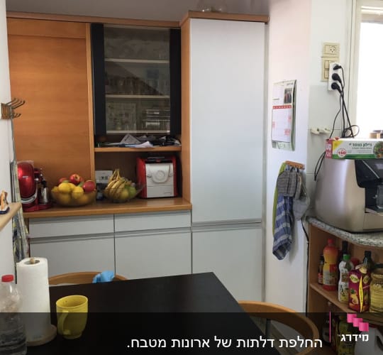 מטבח עם שולחן שחור, כיסאות, ומדפים עם מוצרי מזון.